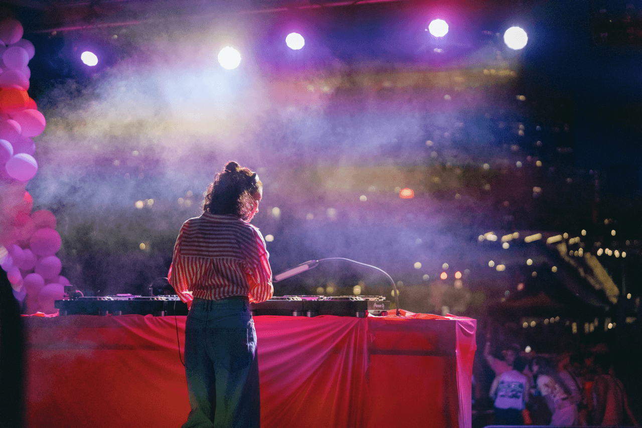A DJ performing to a crowd at night under pink lights.
